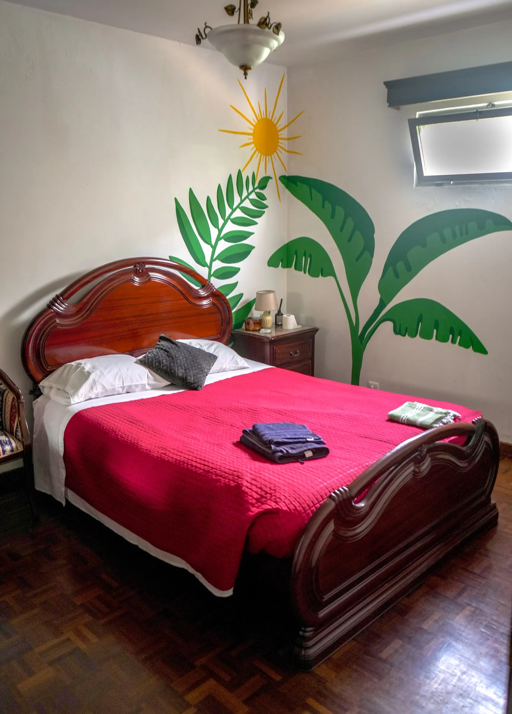 Fusilli wooden double bed with a red cover and banana-leaf mural